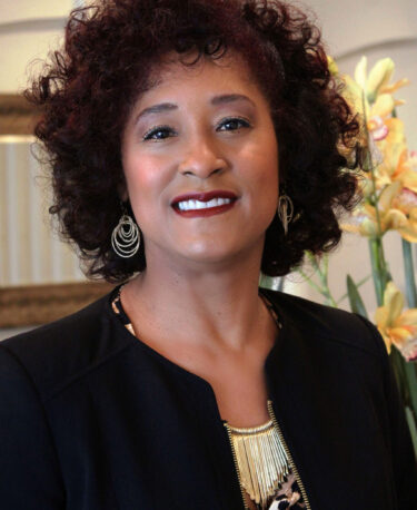 Smiling woman with curly hair wearing earrings and a dark blazer.