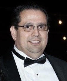 Man in tuxedo and glasses smiling at a formal event.