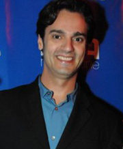 Smiling man in a black blazer and blue shirt at an event.
