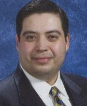 Professional portrait of a man in a suit with a blue background.
