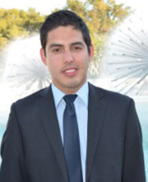 Man in a dark suit and tie smiling outdoors.