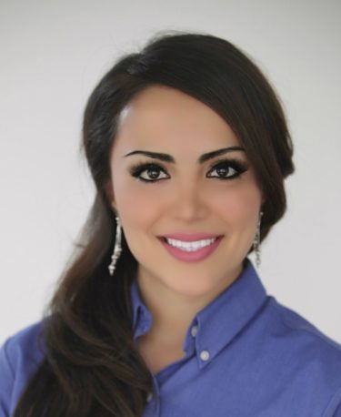 Smiling woman with dark hair in a blue top against a white background.