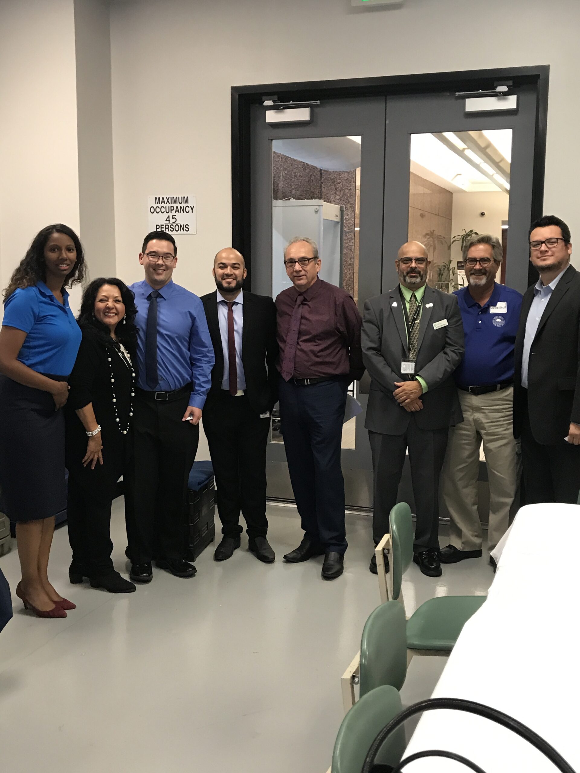 Group of professionally dressed individuals posing indoors, smiling.