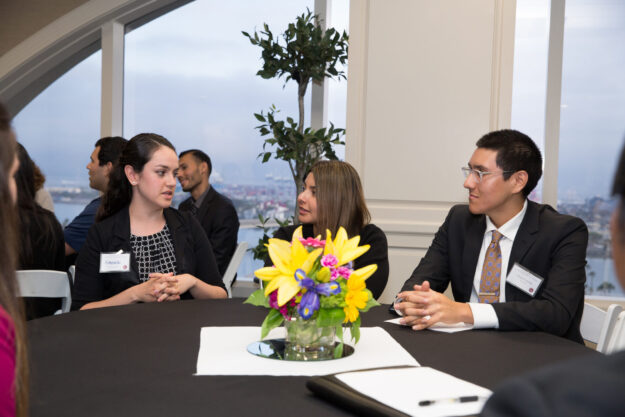 Three professionals engage in a business discussion around a table with a floral centerpiece.